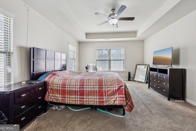 bedroom with a raised ceiling, light carpet, and ceiling fan