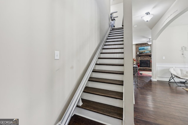 staircase with hardwood / wood-style floors, a stone fireplace, and ceiling fan