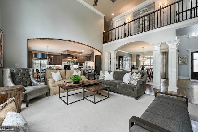 living room with an inviting chandelier, crown molding, a high ceiling, and ornate columns