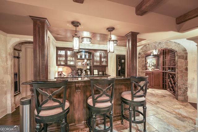 bar with dark stone countertops, hanging light fixtures, decorative columns, and beamed ceiling