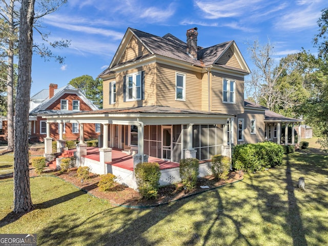 back of property featuring a sunroom, a patio area, and a lawn