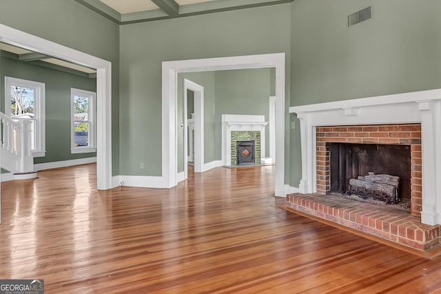 unfurnished living room with beamed ceiling, wood-type flooring, a fireplace, and crown molding