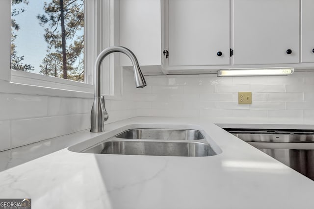 interior details with backsplash, stainless steel dishwasher, sink, and white cabinets