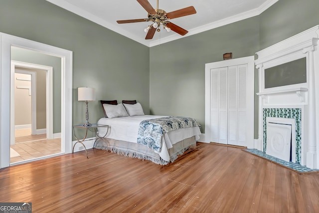 bedroom featuring a tile fireplace, ceiling fan, crown molding, light wood-type flooring, and a closet