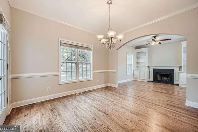 unfurnished living room featuring ornamental molding, ceiling fan with notable chandelier, hardwood / wood-style floors, and built in shelves