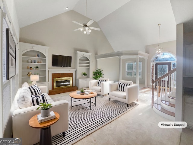 living room featuring a brick fireplace, ceiling fan with notable chandelier, high vaulted ceiling, and built in shelves