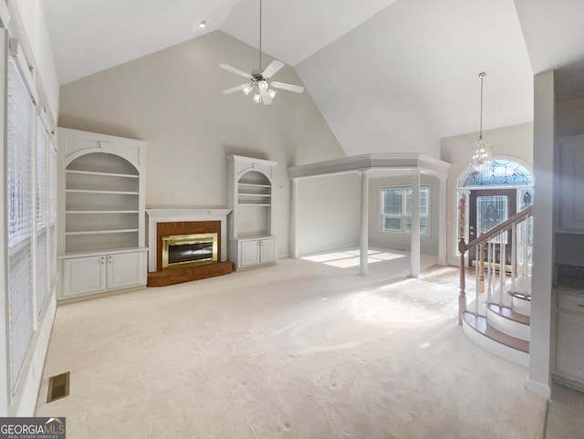 carpeted living room featuring a brick fireplace, ceiling fan with notable chandelier, high vaulted ceiling, and built in shelves