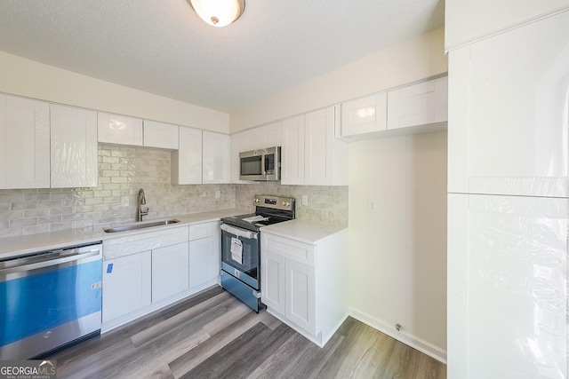 kitchen featuring appliances with stainless steel finishes, white cabinetry, wood-type flooring, sink, and decorative backsplash