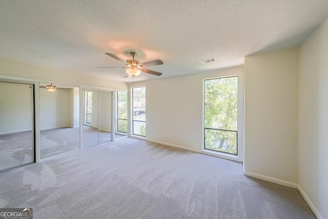 unfurnished bedroom with light carpet, a textured ceiling, multiple windows, and ceiling fan