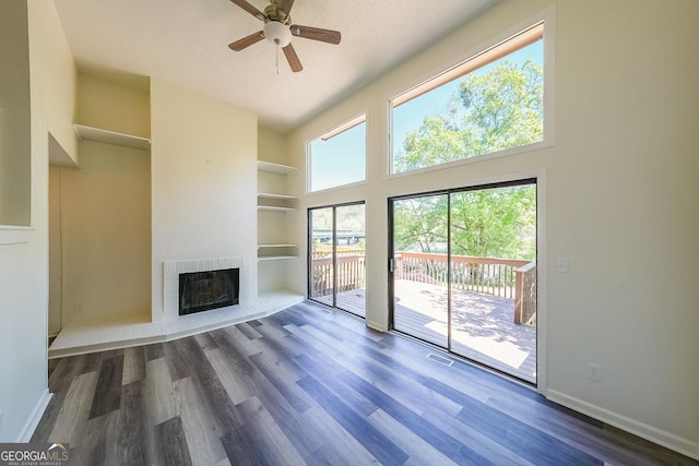 unfurnished living room featuring a healthy amount of sunlight, built in shelves, a fireplace, and dark wood-type flooring