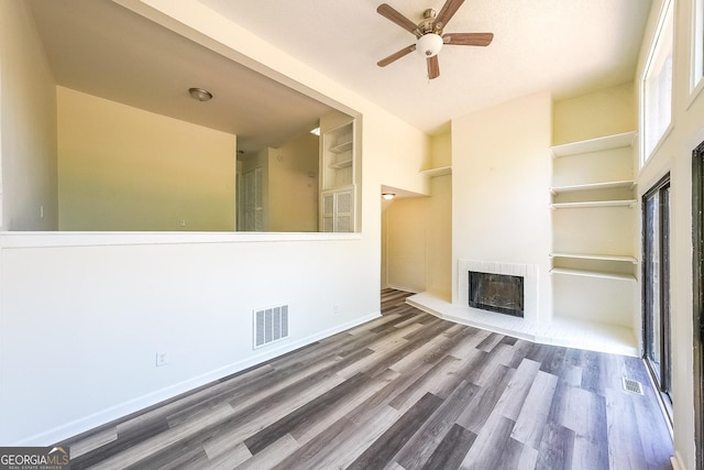 unfurnished living room with built in shelves, ceiling fan, wood-type flooring, and a fireplace