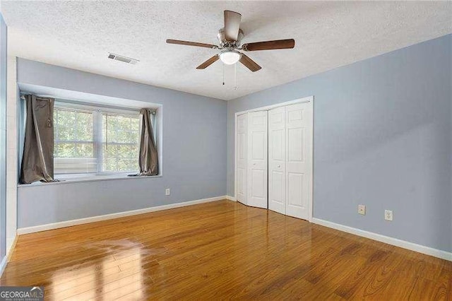 unfurnished bedroom with ceiling fan, wood-type flooring, a closet, and a textured ceiling