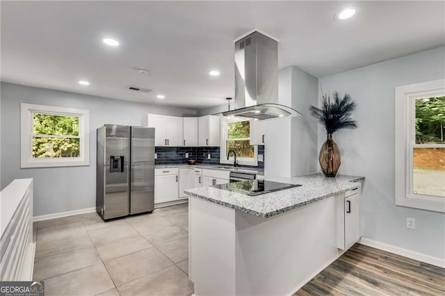 kitchen with white cabinetry, stainless steel fridge, kitchen peninsula, island exhaust hood, and light stone countertops