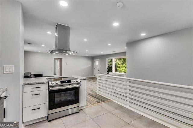 kitchen featuring stainless steel electric range oven, ventilation hood, white cabinetry, light tile patterned floors, and light stone countertops