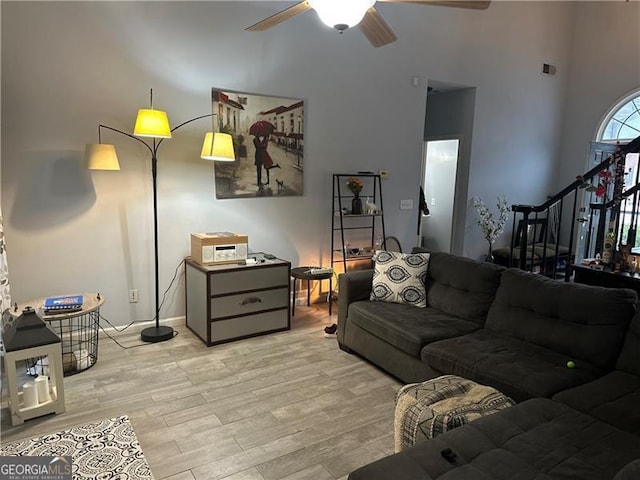 living room featuring a towering ceiling, light hardwood / wood-style flooring, and ceiling fan