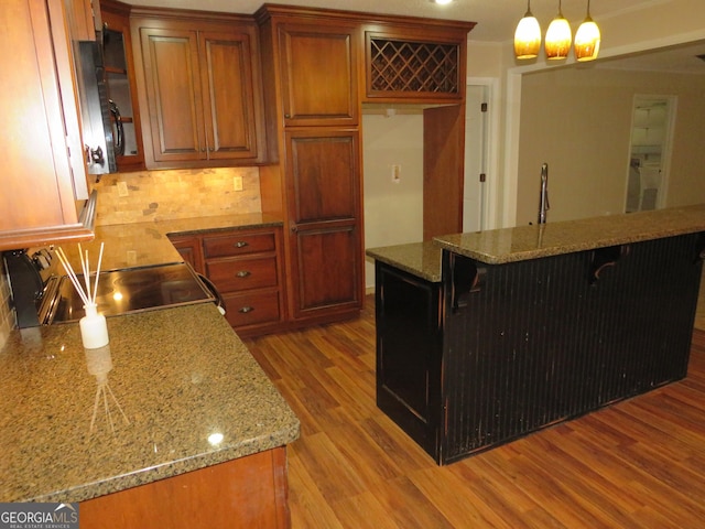 kitchen featuring a breakfast bar area, range, hanging light fixtures, backsplash, and light wood-type flooring