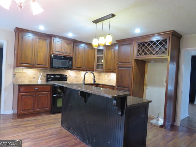 kitchen featuring a breakfast bar, a kitchen island with sink, hanging light fixtures, dark stone countertops, and black appliances