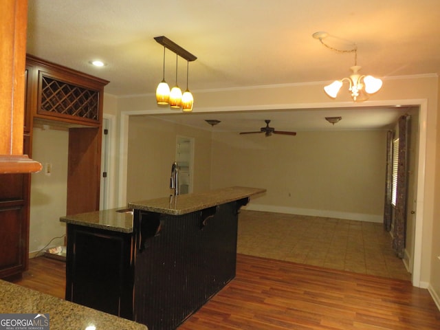 kitchen with dark wood-type flooring, a kitchen bar, crown molding, stone countertops, and pendant lighting