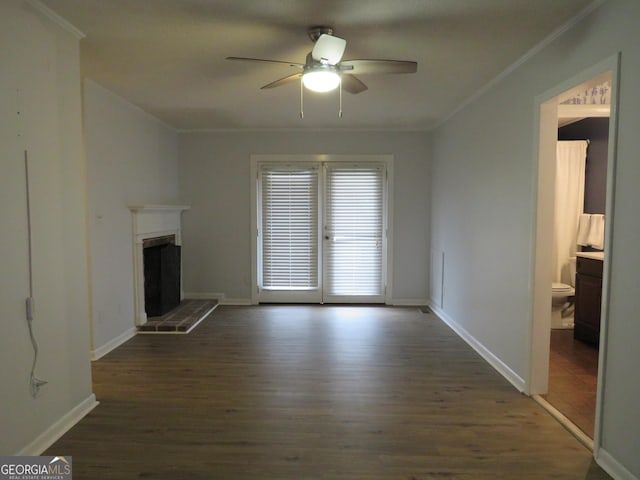 unfurnished living room with a brick fireplace, dark wood-type flooring, ornamental molding, and ceiling fan