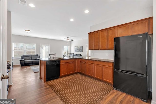 kitchen with hardwood / wood-style flooring, kitchen peninsula, sink, and black appliances