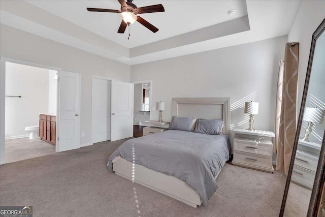 carpeted bedroom featuring a raised ceiling, ceiling fan, and ensuite bath