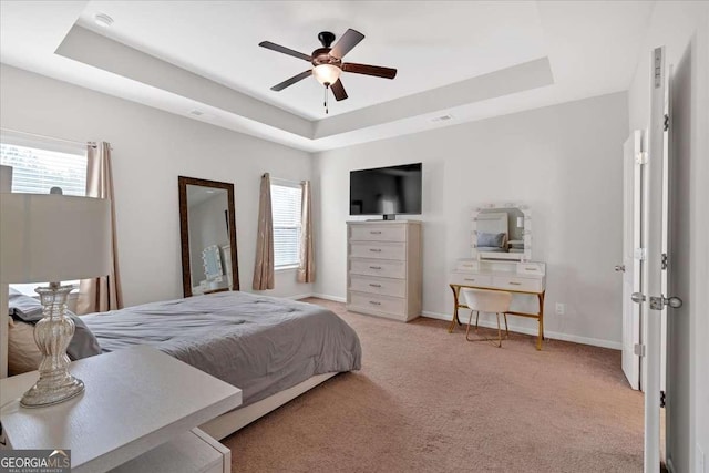 carpeted bedroom with multiple windows, a raised ceiling, and ceiling fan