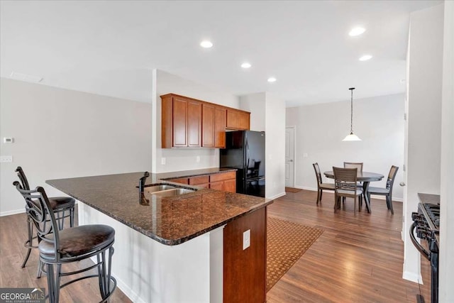 kitchen featuring sink, stainless steel gas range oven, hanging light fixtures, black refrigerator, and kitchen peninsula