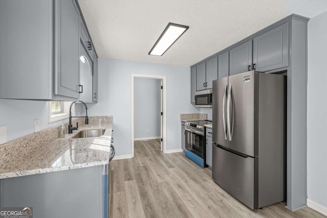 kitchen with gray cabinets, sink, light stone counters, stainless steel appliances, and a textured ceiling