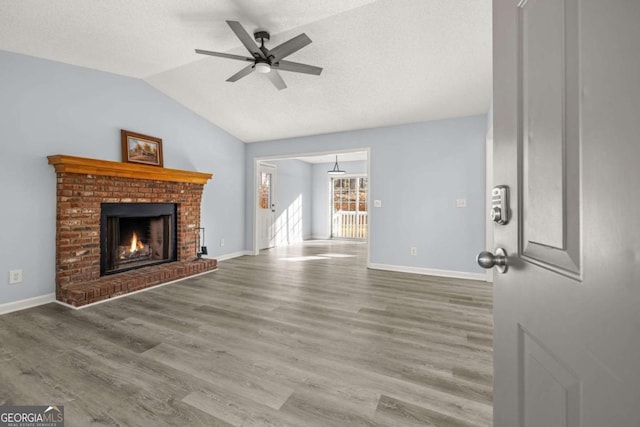 unfurnished living room with lofted ceiling, ceiling fan, wood-type flooring, a fireplace, and a textured ceiling