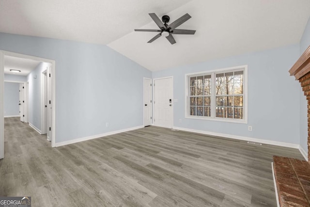 unfurnished living room with wood-type flooring, lofted ceiling, ceiling fan, and a brick fireplace