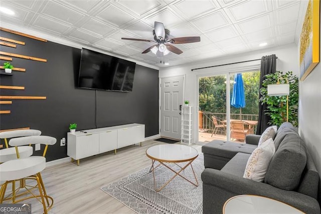 living area featuring a ceiling fan, an ornate ceiling, baseboards, and wood finished floors