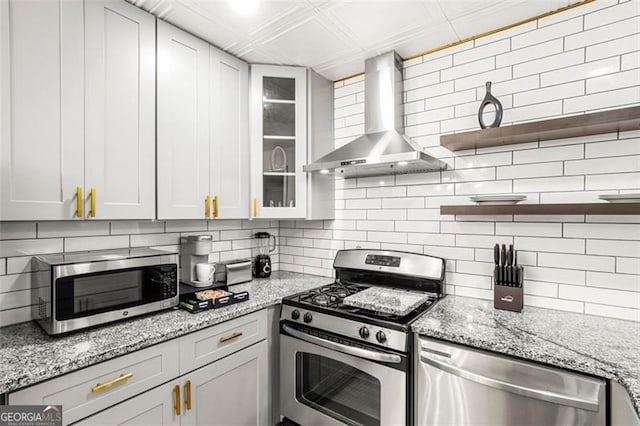 kitchen with white cabinets, backsplash, light stone counters, stainless steel appliances, and wall chimney exhaust hood