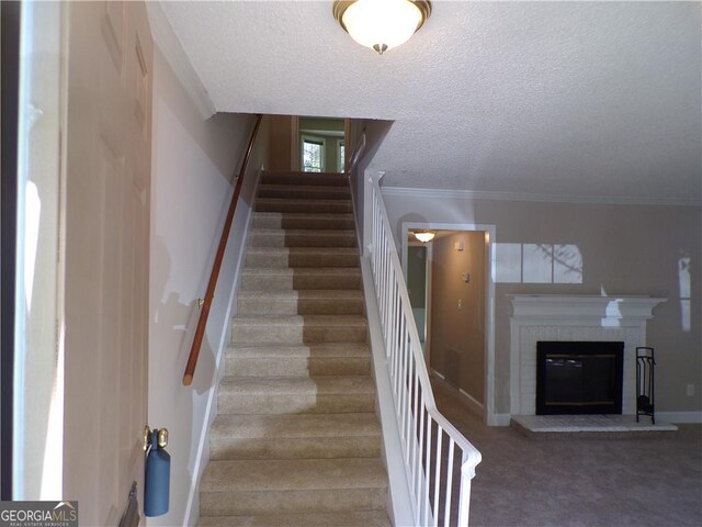 staircase with ornamental molding, a brick fireplace, carpet flooring, and a textured ceiling