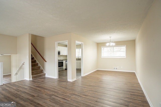 unfurnished living room with a textured ceiling, a notable chandelier, and dark hardwood / wood-style flooring