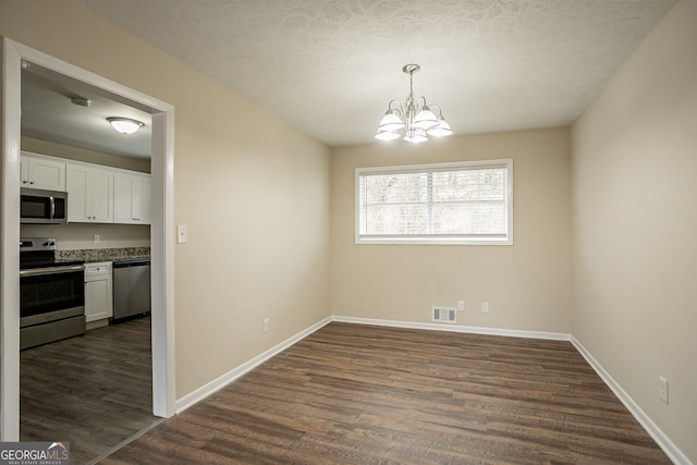 unfurnished dining area featuring an inviting chandelier, a textured ceiling, and dark hardwood / wood-style flooring