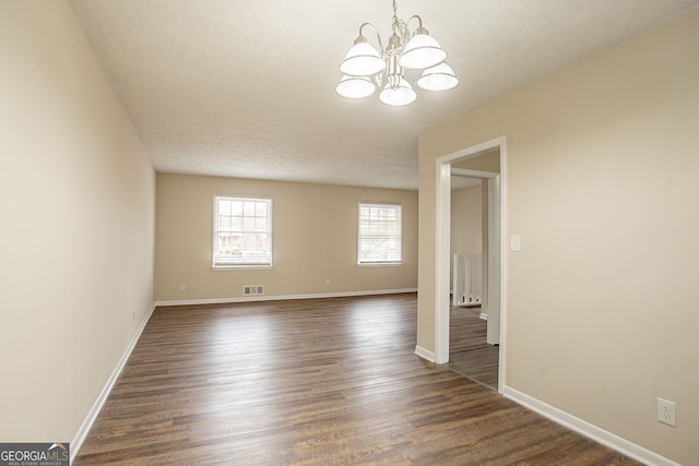 unfurnished room with an inviting chandelier and dark hardwood / wood-style flooring