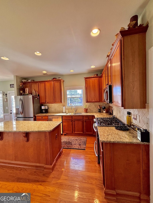 kitchen with a kitchen island, appliances with stainless steel finishes, sink, and light wood-type flooring