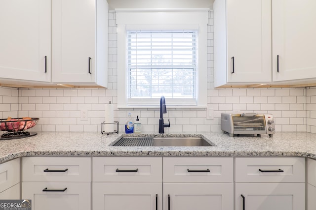 kitchen with light stone counters, sink, backsplash, and white cabinets