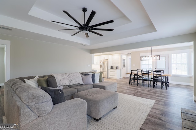 living room featuring a raised ceiling, wood-type flooring, and ceiling fan