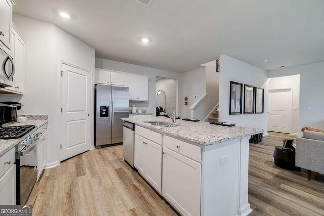 kitchen featuring light hardwood / wood-style flooring, appliances with stainless steel finishes, light stone countertops, an island with sink, and white cabinets