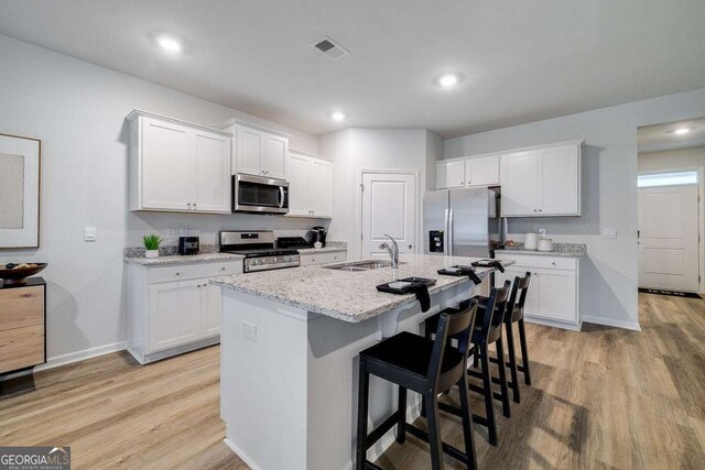 kitchen featuring white cabinetry, sink, stainless steel appliances, and an island with sink