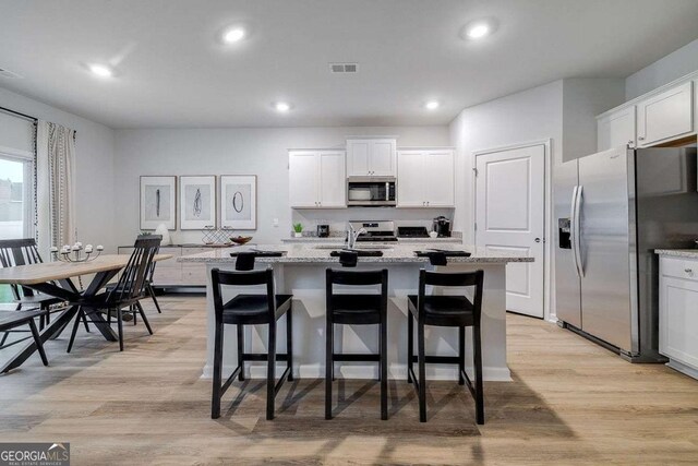 kitchen with appliances with stainless steel finishes, light stone countertops, a kitchen island with sink, and white cabinets