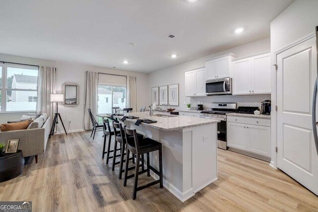 kitchen featuring a kitchen island with sink, white cabinetry, light hardwood / wood-style floors, and appliances with stainless steel finishes