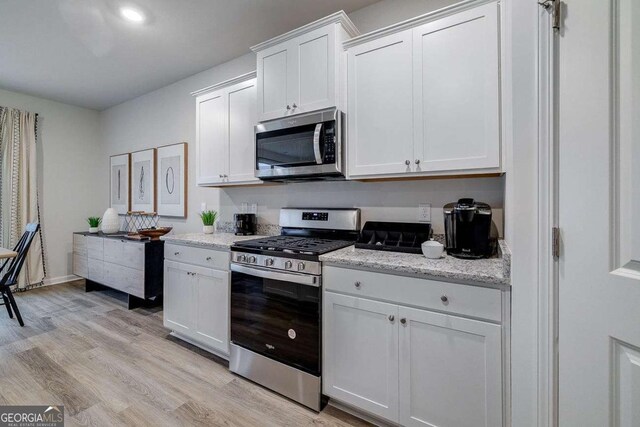 kitchen featuring white cabinetry, light stone counters, light hardwood / wood-style flooring, and stainless steel appliances