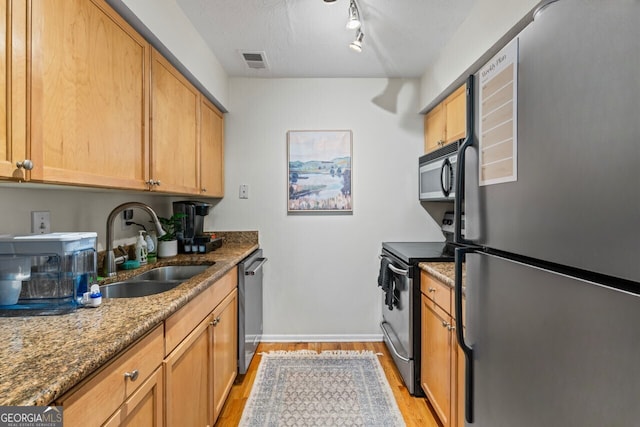 kitchen with sink, a textured ceiling, light wood-type flooring, dark stone countertops, and stainless steel appliances