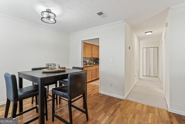 dining room with sink, ornamental molding, a textured ceiling, and light wood-type flooring