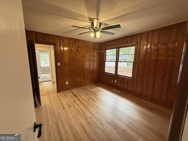 empty room featuring ceiling fan, light wood-type flooring, a textured ceiling, and wood walls