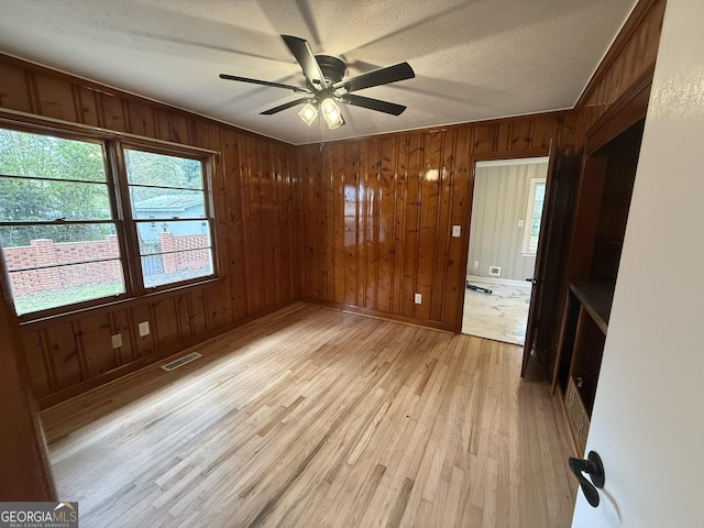 empty room with a textured ceiling, wood walls, ceiling fan, and light hardwood / wood-style flooring