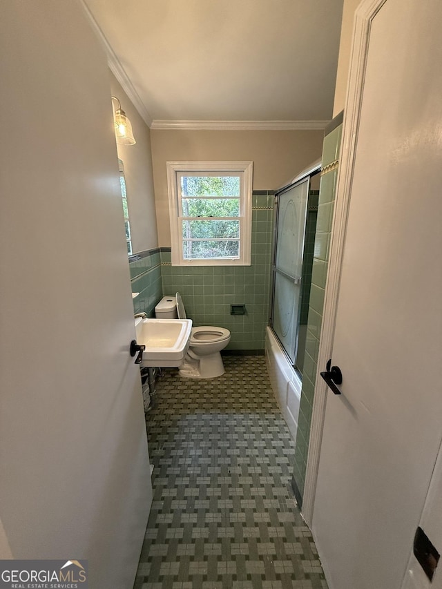 full bathroom with bath / shower combo with glass door, ornamental molding, toilet, and tile walls