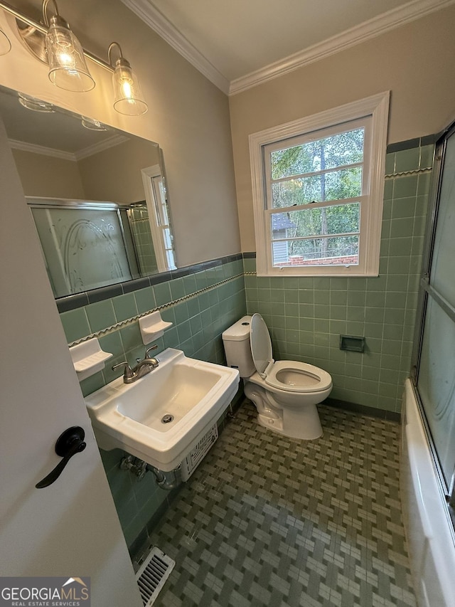 full bathroom with sink, combined bath / shower with glass door, tile walls, ornamental molding, and toilet